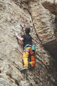 男子专注攀爬裸露岩壁，橙色裤装与安全带凸显专业装备