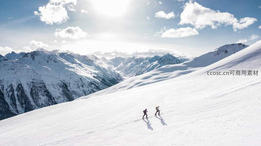 两人踏雪前行，身影映衬雪山之巅