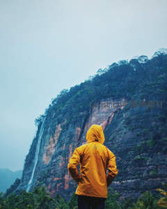 雨衣旅人仰望瀑布与赤色崖壁