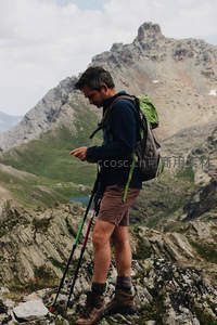 登山者倚杖查看手机，身后是雄伟山峦