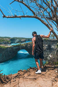 悬崖观景台，男子手扶枯枝眺望海蚀拱门