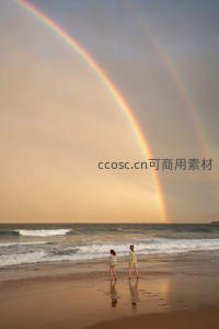双彩虹下情侣漫步金色沙滩