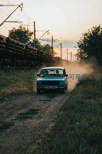 蓝色老式汽车扬起尘土，驶过铁轨旁乡间小路
