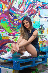 女孩坐于涂鸦墙前蓝色托盘上微笑