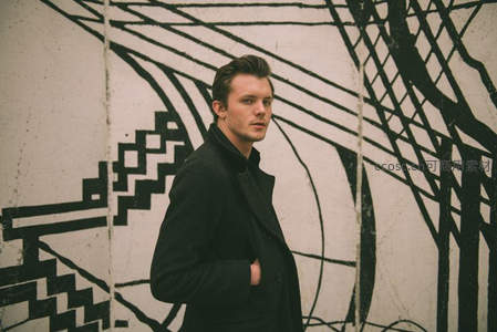 黑衣男子倚靠涂鸦墙的时尚街拍