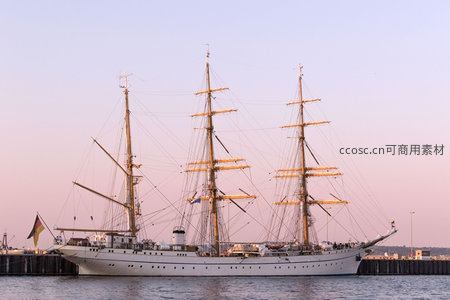 三桅帆船静泊港湾夕阳余晖中