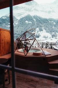 雪山温泉木屋中的女子，窗外是壮丽雪峰与森林