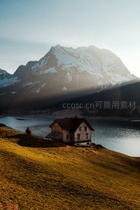 湖畔小屋沐晨光，雪峰倒影波光粼，山影斜射如画境