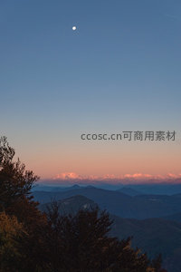 月升山巅映雪峰，暮霭层叠绘出诗意天际线