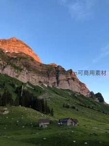夕阳余晖映照山体，牧屋静卧翠绿山坡之上