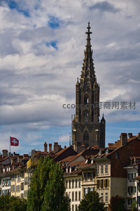 伯尔尼明斯特大教堂尖塔刺破云层，红瓦屋顶与瑞士国旗飘扬