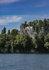 湖畔古堡隐于翠林间，石砌塔楼映蓝天白云