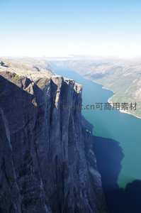 悬崖绝壁俯瞰碧蓝峡湾，巨岩嶙峋直插水面，光影勾勒壮阔地质奇观