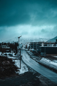 雪后城市街道蜿蜒上山，起重机矗立，现代建筑群隐于雾霭山峦之下