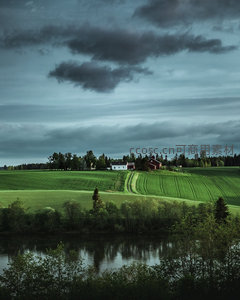 河畔远眺：层叠绿野与红顶农舍在暮色云层下静谧伫立