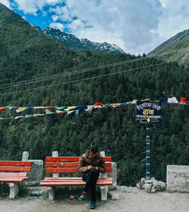 喜马拉雅山脚下旅人静坐红椅，经幡飘扬，远山雪峰苍翠林海环绕