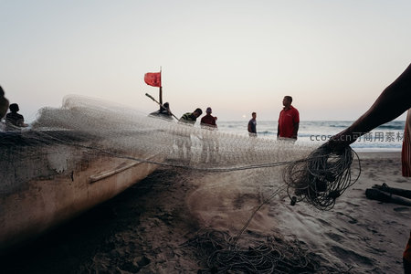 渔民清晨收网归岸，小船搁浅沙滩，红帆映衬海天微光