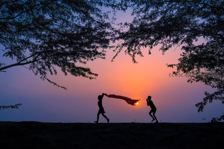 夕阳下孩童奔跑挥舞红布，剪影映衬绚丽晚霞与树影