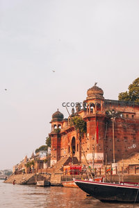 恒河岸边古庙群与停泊木船，飞鸟掠过红砂岩建筑群