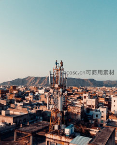 通信塔顶工人作业，俯瞰密集老城区与远山剪影的黄昏景象