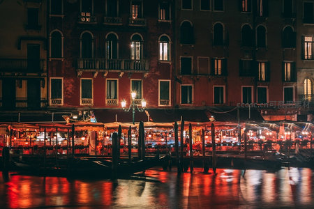 威尼斯夜色码头灯火辉煌，红色霓虹倒影水中，贡多拉静泊岸边如诗如画