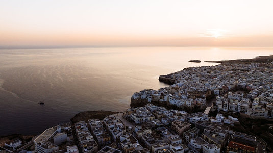航拍视角下白城依崖而建，夕阳洒金海面与密集屋群交相辉映