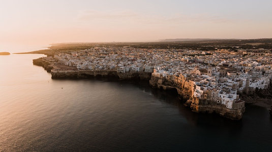 金色夕照中的悬崖古城全景，白屋群沿崎岖海岸线蜿蜒伸展