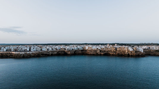 平视视角下的海岸古城静谧清晨，白墙灰瓦与深蓝海水形成冷暖对比