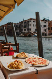 威尼斯河畔餐厅户外餐桌，意面披萨配水城拱桥背景