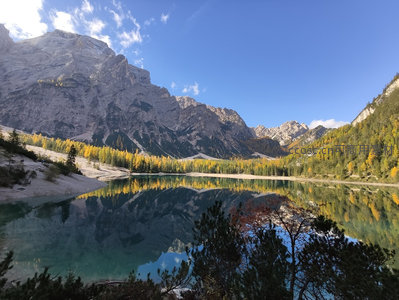 秋日高山湖泊倒影，金黄林带映衬巍峨岩壁与澄澈碧水