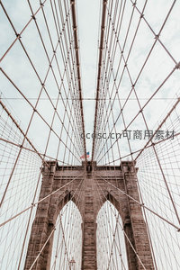 仰望布鲁克林大桥钢索交织穹顶，石塔雄浑，星条旗飘扬