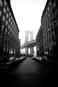 黑白街巷尽头，曼哈顿大桥隐现雾中，老楼与车影诉说城市记忆