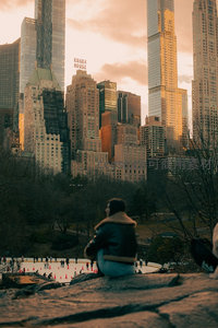 黄昏时分中央公园冰场旁，游客凝望金色余晖洒落曼哈顿高楼群与埃塞克斯大厦招牌