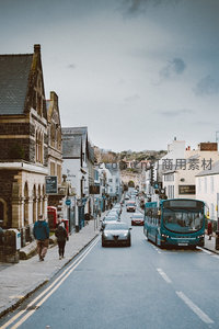 坡道小镇街道车流穿梭，青绿色巴士与石砌建筑构成宁静英伦风情