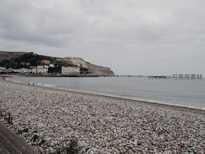 阴云笼罩下的卵石海滩与远处山崖城镇全景