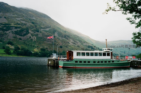 湖畔绿白游船停靠码头，背景青山云雾缭绕，英国国旗飘扬
