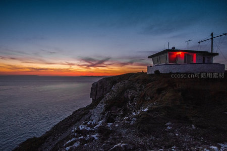 悬崖灯塔日落时分，红光映照海天交界处