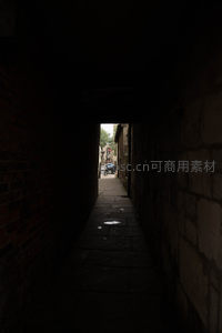 幽暗拱廊通道尽头透光，石墙缝隙间窥见街市一角