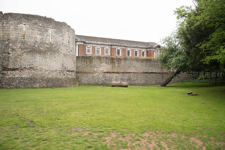 古老石砌城墙与红砖建筑并立，绿茵草地映衬历史沧桑感