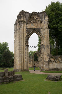 哥特式教堂拱门废墟矗立绿茵中，游人穿行其间感受时光流逝