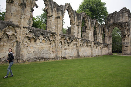 女子漫步于修道院残垣断壁间，连续飞扶壁与尖拱诉说昔日辉煌