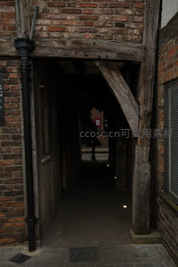 古砖木结构巷道入口，昏暗光影中行人剪影若隐若现