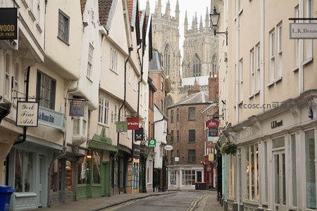 约克窄街远眺大教堂尖塔，两旁店铺林立招牌错落有致
