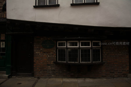 昏暗光影下的都铎式砖墙老屋，绿色门牌诉说岁月故事