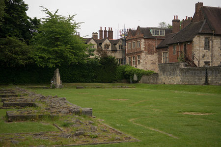 绿茵草坪上散落古墓石基，背景是连排红砖石砌老屋与茂密树丛