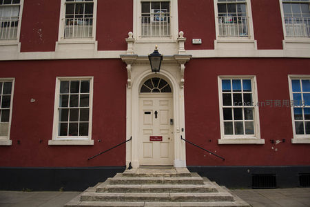 红墙白窗古典英式建筑入口，门楣雕饰与铁艺灯盏典雅