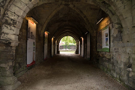 古老石拱廊道内展板林立，尽头绿树掩映庭院入口