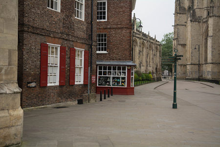 红窗砖墙小屋毗邻教堂回廊，街角红色售货亭陈列精致商品