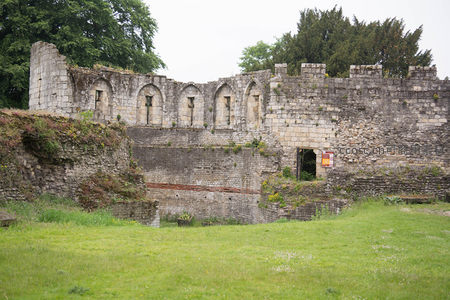 中世纪城堡遗址嵌入绿野，石墙拱窗爬满藤蔓，入口处立有解说牌