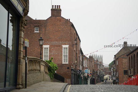 约克老街坡道远景，红砖建筑林立，彩旗悬空，远处大教堂尖顶隐约可见